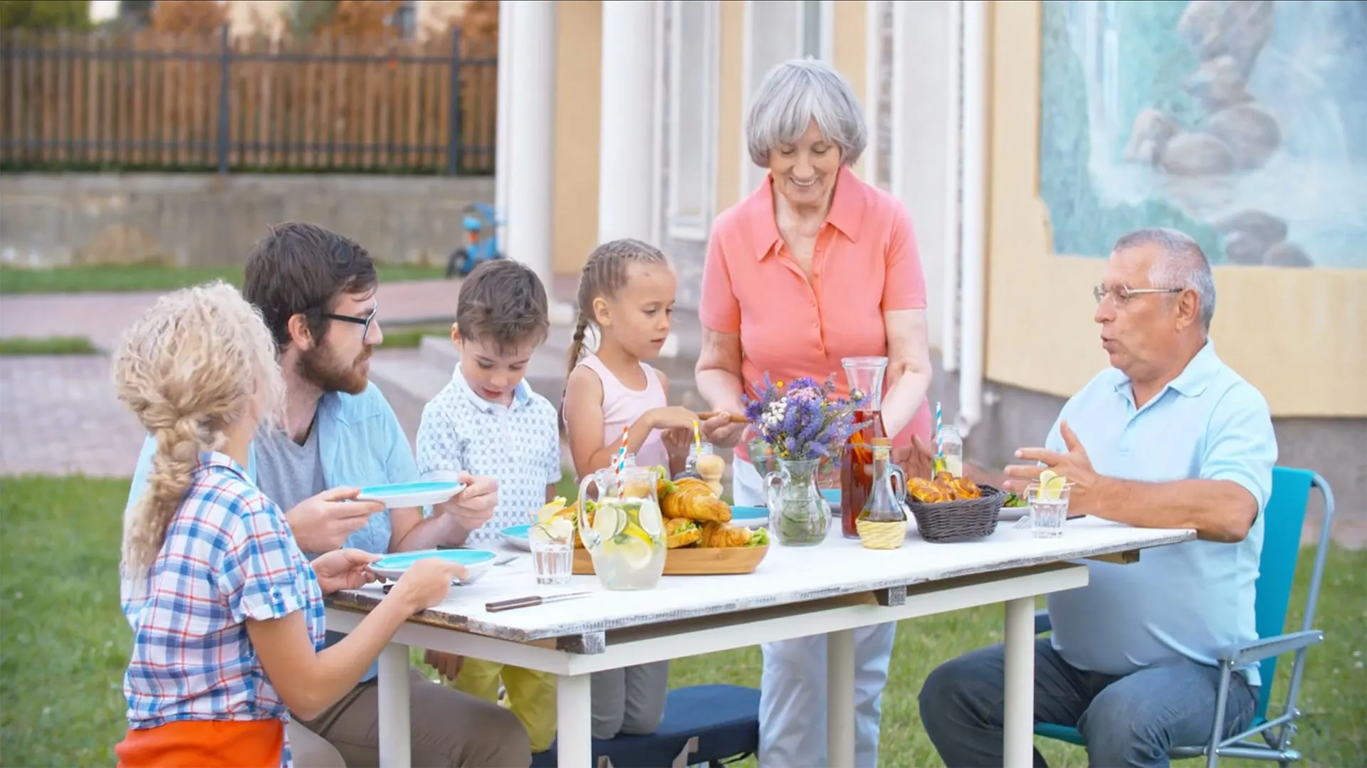Família de três gerações à mesa, num almoço no jardim